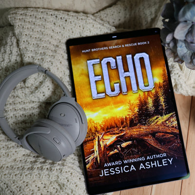 A tablet displaying the book cover of 'ECHO' by Jessica Ashley, styled on a beige knit blanket next to gray over-ear headphones and a dried flower.