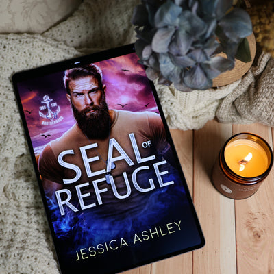 A tablet lying on a wooden surface displays the book cover for 'Seal of Refuge' by Jessica Ashley. The scene is styled with a knitted blanket, a potted plant, and a lit candle.